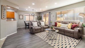 A modern living room with a brown leather sofa, a glass coffee table, and a dining area with a table and chairs. - Casa Aria 4br Home & Heated Pool 4 Bedroom Home (Casa Grande)