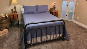 A bedroom with a bed, two nightstands, a wall sign, a door, and a carpeted floor. - Step Back In Time to a charming 2-bedroom lower level house in adorable Eudora (Eudora)