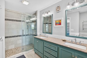 A bathroom with a glass shower enclosure, a large mirror, and a sink with a vanity.