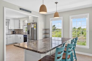 Una cocina con armarios blancos, encimera de granito, refrigerador de acero inoxidable y una zona de comedor con sillas azules.
