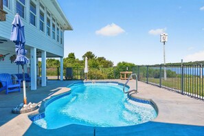 Una piscina con borde de azulejos, un área de estar cubierta con sillas azules y vista a un cuerpo de agua.