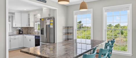 A modern kitchen with white cabinets, a stainless steel refrigerator, and a large island with blue chairs.