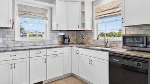 A modern kitchen with white cabinetry, a built-in dishwasher, a coffee maker, and a microwave. - Island Time 3 Bedroom Home (Supply)