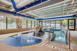 Ein Hallenbad mit Whirlpool, Wasserrutsche und Blick ins Freie.