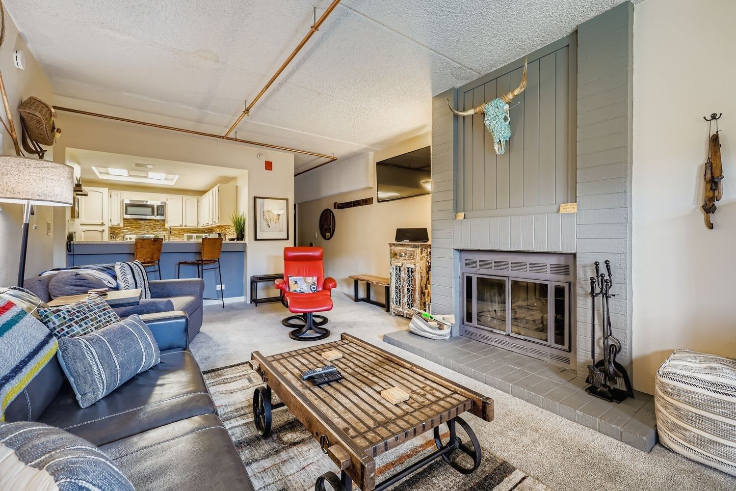 A cozy living room with a fireplace, a sofa, a red chair, and a coffee table.