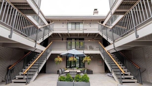 A modern building with a central courtyard featuring a dining area with outdoor furniture and a table, surrounded by planters. There are two staircases on either side, leading to upper levels. - Aspen Downtown 2BR Ski Condo w/ Fireplace - CD 17 (Aspen)