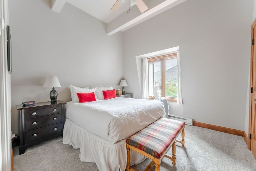 Une chambre à coucher avec un lit, des tables de chevet, un banc et une fenêtre.