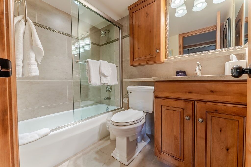 A bathroom with a glass-enclosed shower, a bathtub, a toilet, wooden cabinets, and a mirror.