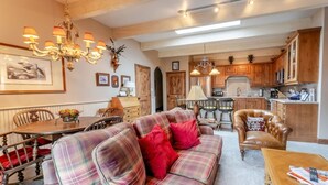 A cozy living room with a plaid sofa, red pillows, and a dining table with chairs. There is a kitchen in the background with wooden cabinets and a chandelier. - Aspen Downtown 2BR Ski Condo w/ Fireplace - CD 17 (Aspen)