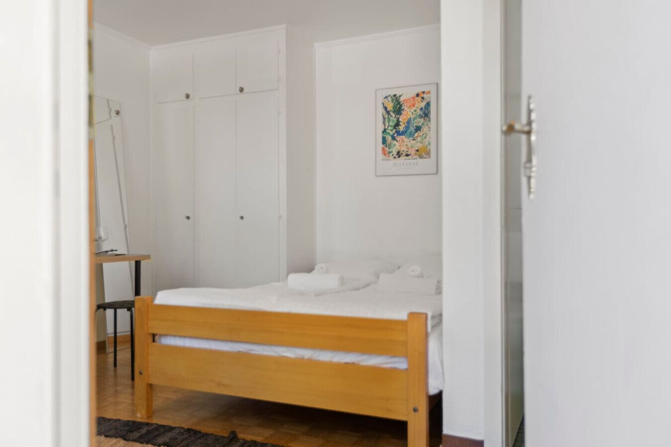 Une chambre avec un lit en bois, une armoire blanche et un tableau abstrait encadré accroché au mur.
