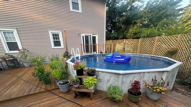An outdoor swimming pool with a wooden deck, surrounded by potted plants and a wooden fence. - Charming 4 Bedroom, Fire Pit, Outdoor Projector, Heated Pool, Close to Downtown (Washington)