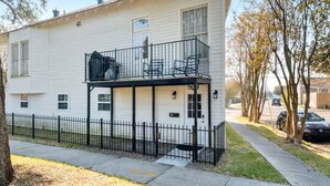 Un bâtiment blanc à deux étages, doté d’un balcon, d’une cour clôturée et d’une voiture garée.