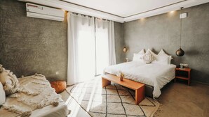Un dormitorio moderno con cama, mesita de noche, banco y un ventanal con cortinas.