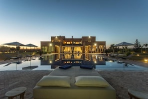 A modern hotel with a swimming pool, lounge chairs, and a well-lit interior.