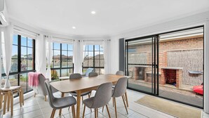 A dining area with a large table and chairs, a view of a brick wall and outdoor seating, and a glass door leading outside. - 17 Matthew Flinders Dve Encounter Bay (Encounter Bay)