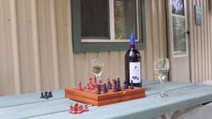 A wooden chessboard with pieces, a bottle of wine, and two glasses of wine on a table.