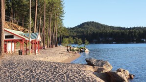 A beach with a wooden structure, a clear view of the water, and a forested hill in the background.