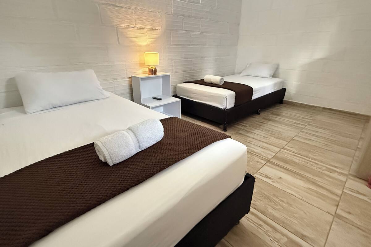 A hotel room with two beds, a nightstand with a lamp, and a brick wall.