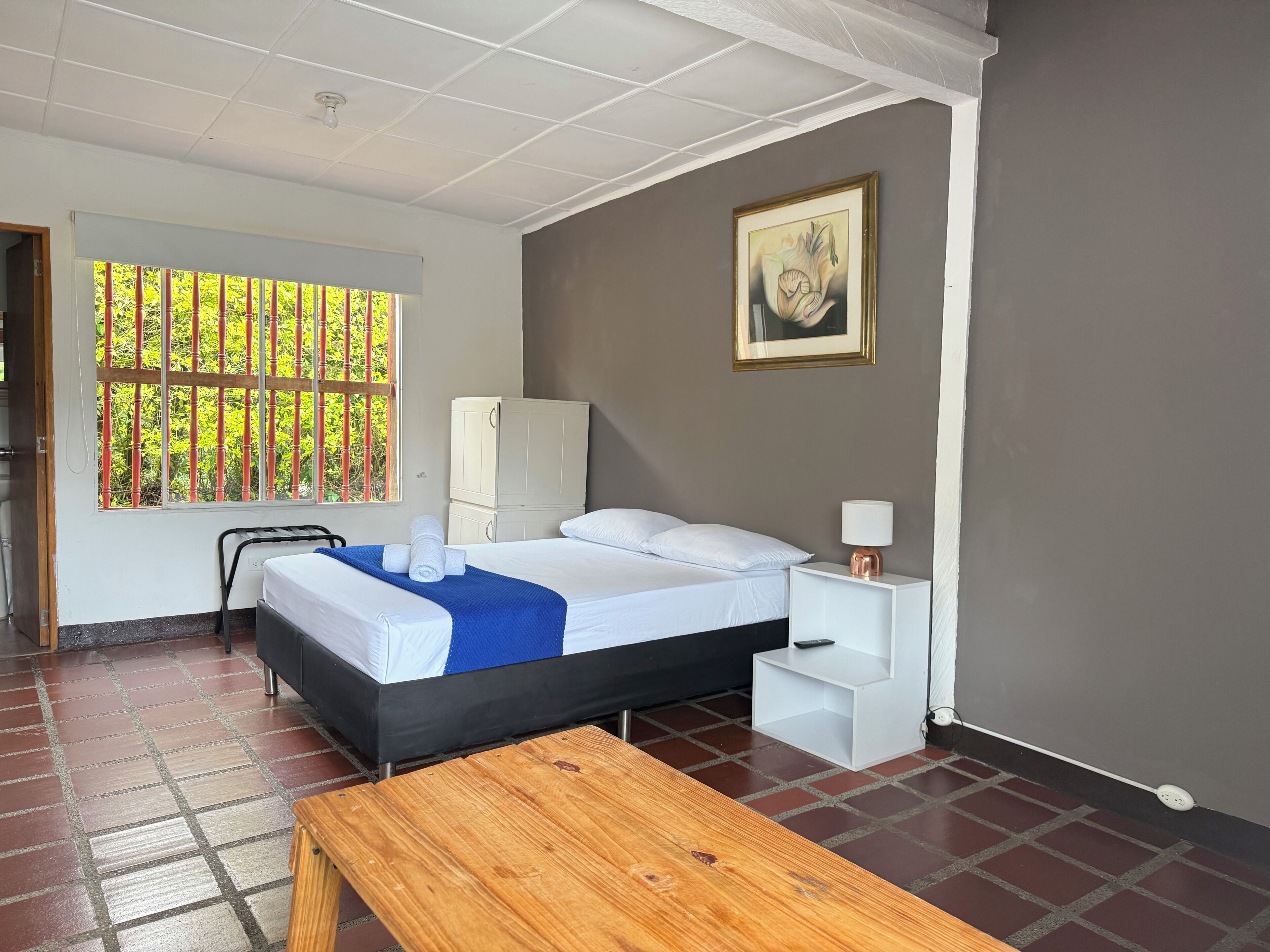 Una habitación de hotel con cama, mesita de noche, lámpara y un cuadro en la pared.