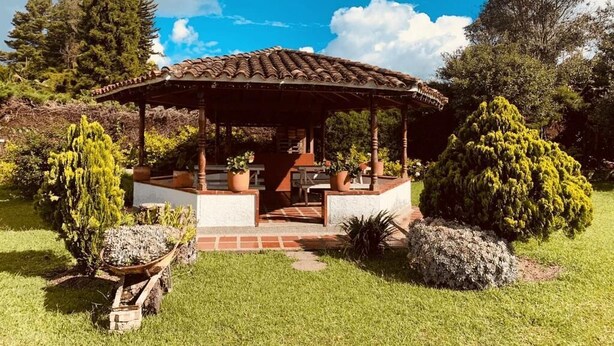 A gazebo with a tiled roof, surrounded by potted plants and rocks, set in a grassy area with trees in the background. - Hotel CSI Llanogrande (Rionegro)