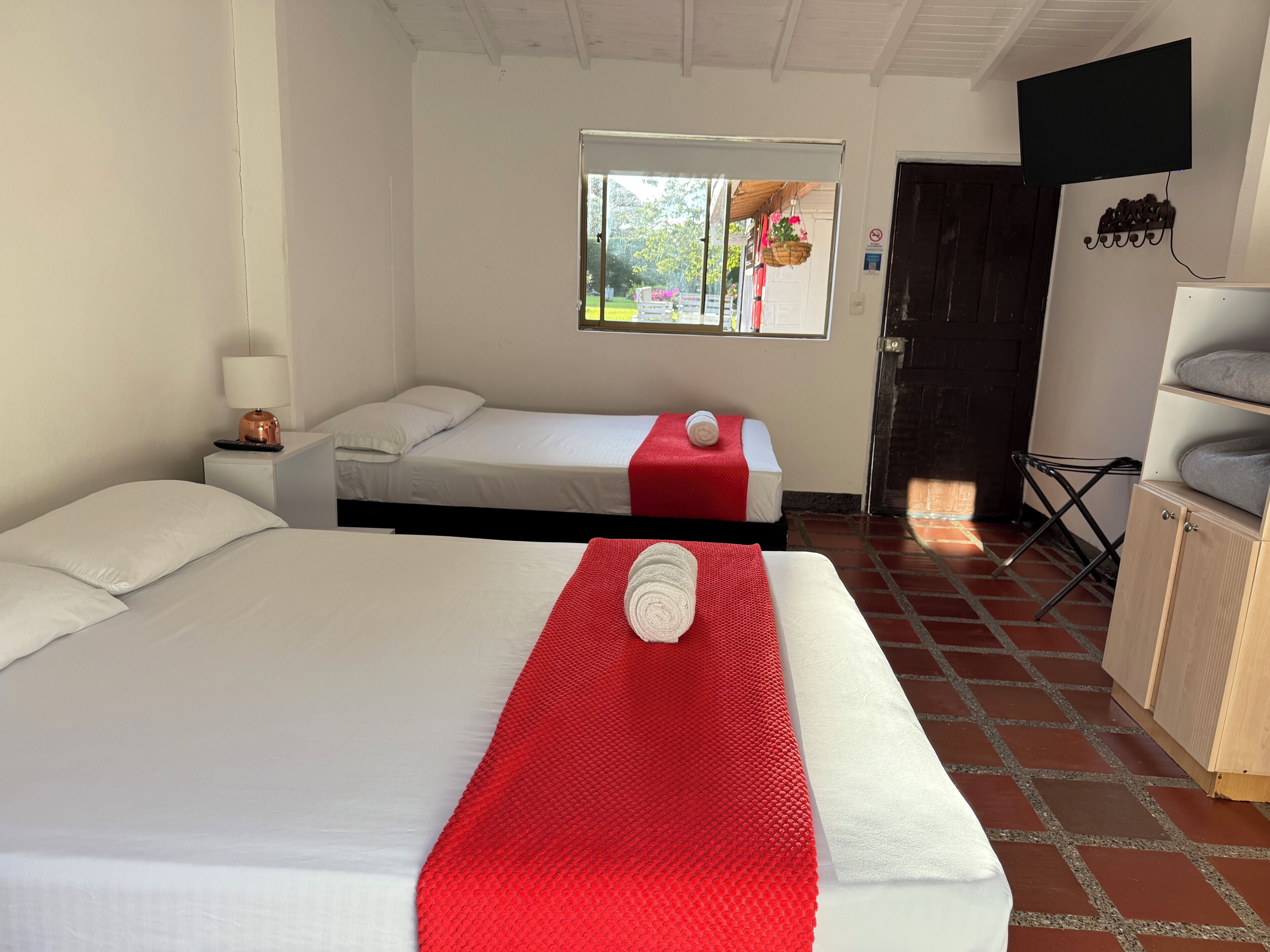 A room with two beds, a window with a view, a TV mounted on the wall, and a small cabinet.