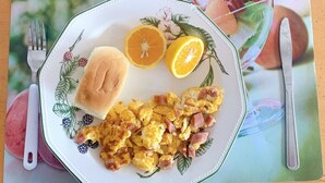 A plate with scrambled eggs, ham, and a slice of orange on a floral placemat. - Hotel CSI Llanogrande (Rionegro)
