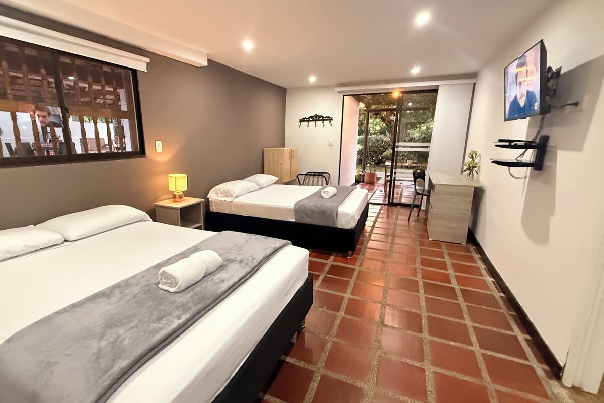 A hotel room with two beds, a desk, a chair, a TV, and a view of the outdoors.