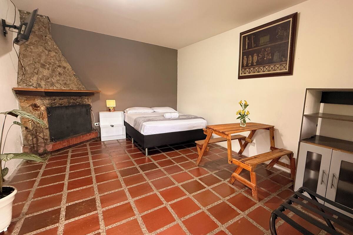 A bedroom with a fireplace, a bed, a nightstand, a wooden table, and a cabinet.