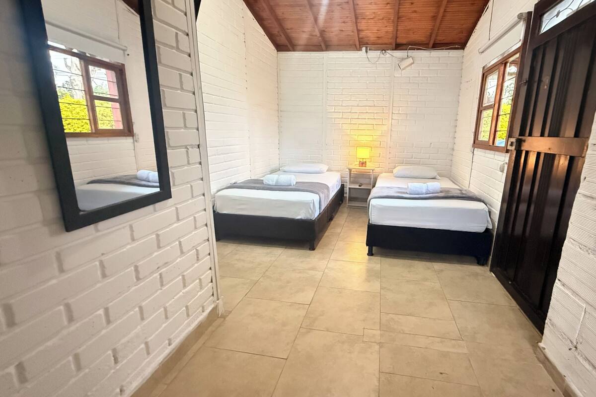 A corridor leading to two single beds with a nightstand between them, a mirror on the left, and a wooden door on the right.