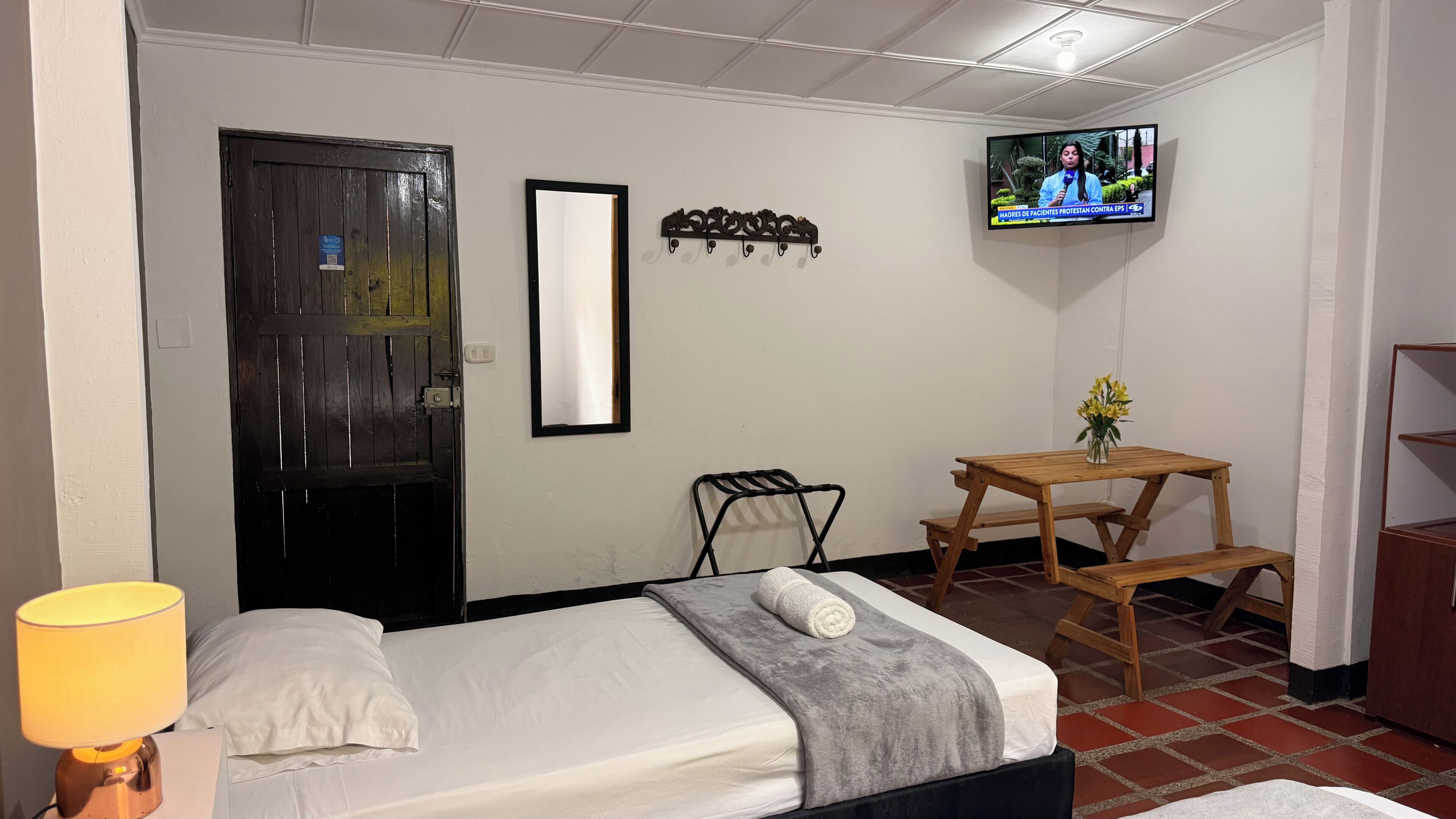 Quarto de hotel com cama, televisão, escrivaninha, cadeira e abajur.