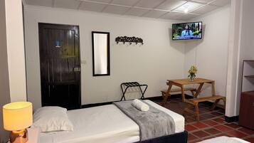 Quarto de hotel com cama, televisão, escrivaninha, cadeira e abajur.