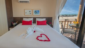 A hotel room with a bed, red and white pillows, a heart-shaped decoration, and a balcony with a view of the beach. - Sumatera House (Trairi)