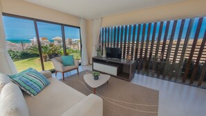 A modern living room with a sofa, coffee table, and TV stand, large windows with a view of the beach and ocean. - Sumatera House (Trairi)