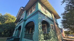 A two-story house with a steeply pitched roof, multiple windows, and a porch with a railing. - Historic Southtown Oasis (San Antonio)