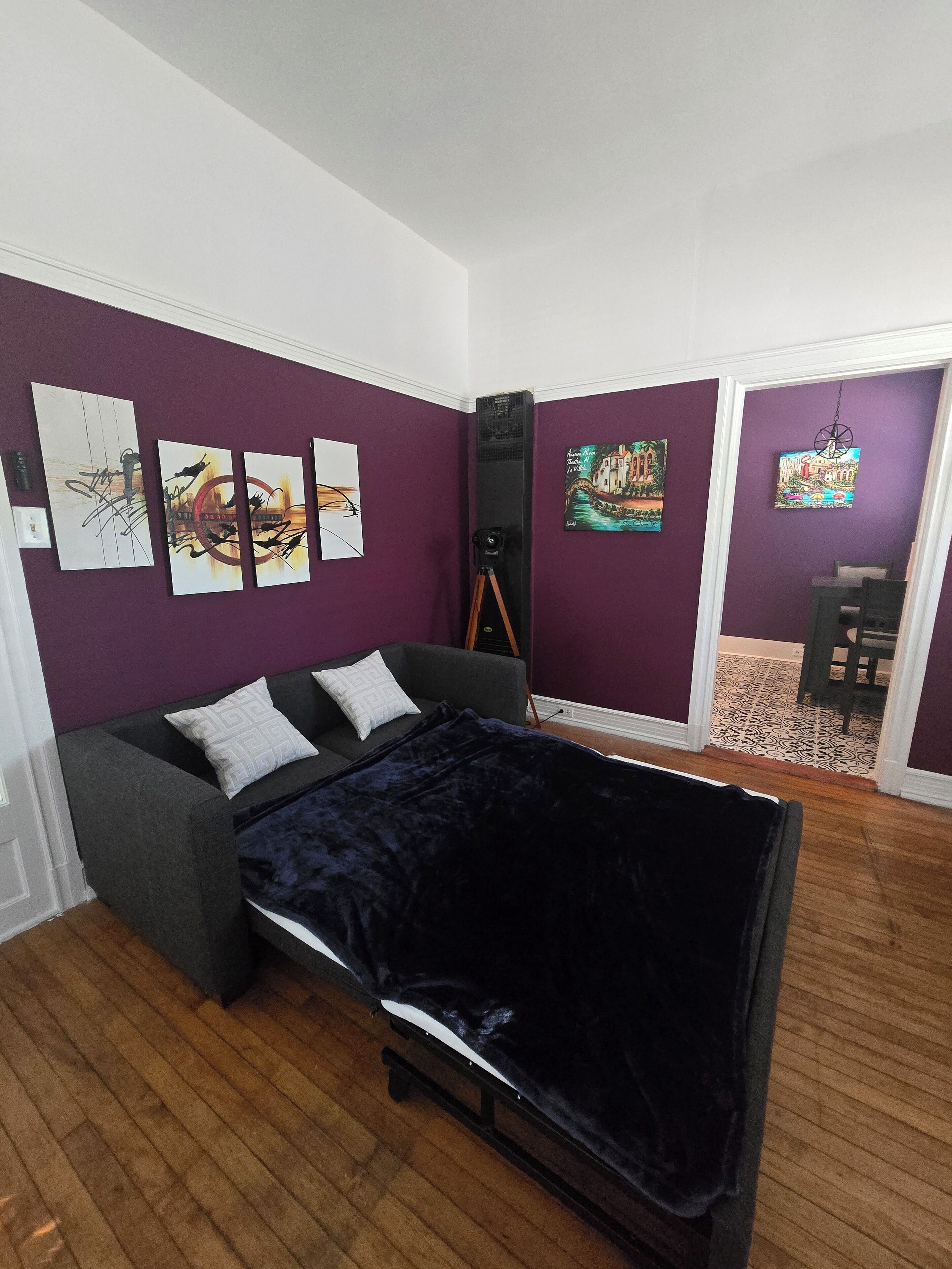 A bedroom with a bed, a couch, and a camera on a tripod.