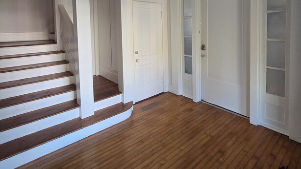 A spacious room with wooden flooring, white walls, and a staircase leading to another level. - Historic Southtown Oasis (San Antonio)