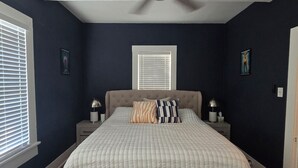 A bedroom with a bed, a ceiling fan, a window with blinds, and a nightstand with a lamp. - Historic Southtown Oasis (San Antonio)