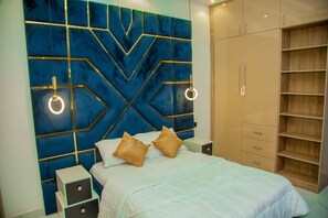 A bedroom with a bed, bedside tables, a wardrobe, and a decorative wall panel. - Aviv Luxury Homes (Enugu)