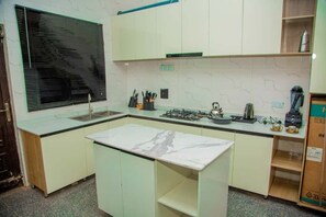 A compact kitchen with a marble countertop, a gas stove, and a sink. - Aviv Luxury Homes (Enugu)
