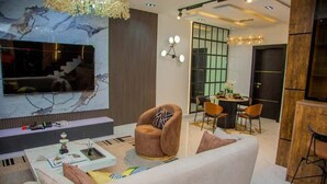 Una sala de estar moderna con un sofá cómodo, una mesa de centro y un televisor montado en una pared de mármol. Hay una zona de comedor con una mesa y sillas, y un mueble de madera.