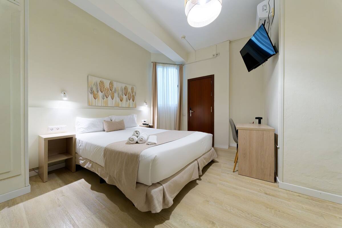 A neatly arranged hotel room with a bed, bedside table, lamp, and a TV mounted on the wall.