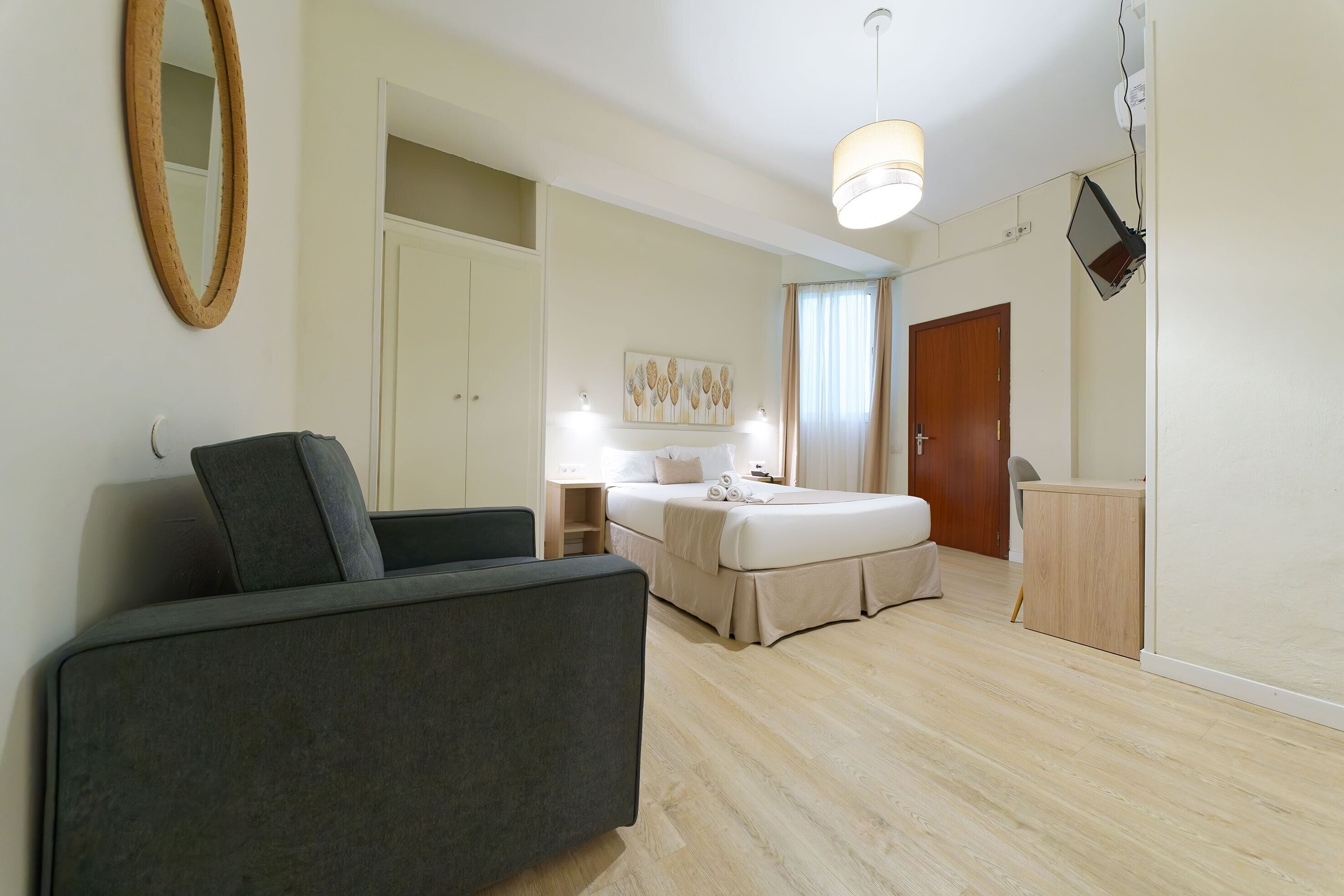 A modern hotel room with a sofa, a bed with a canopy, a desk, and a mirror.