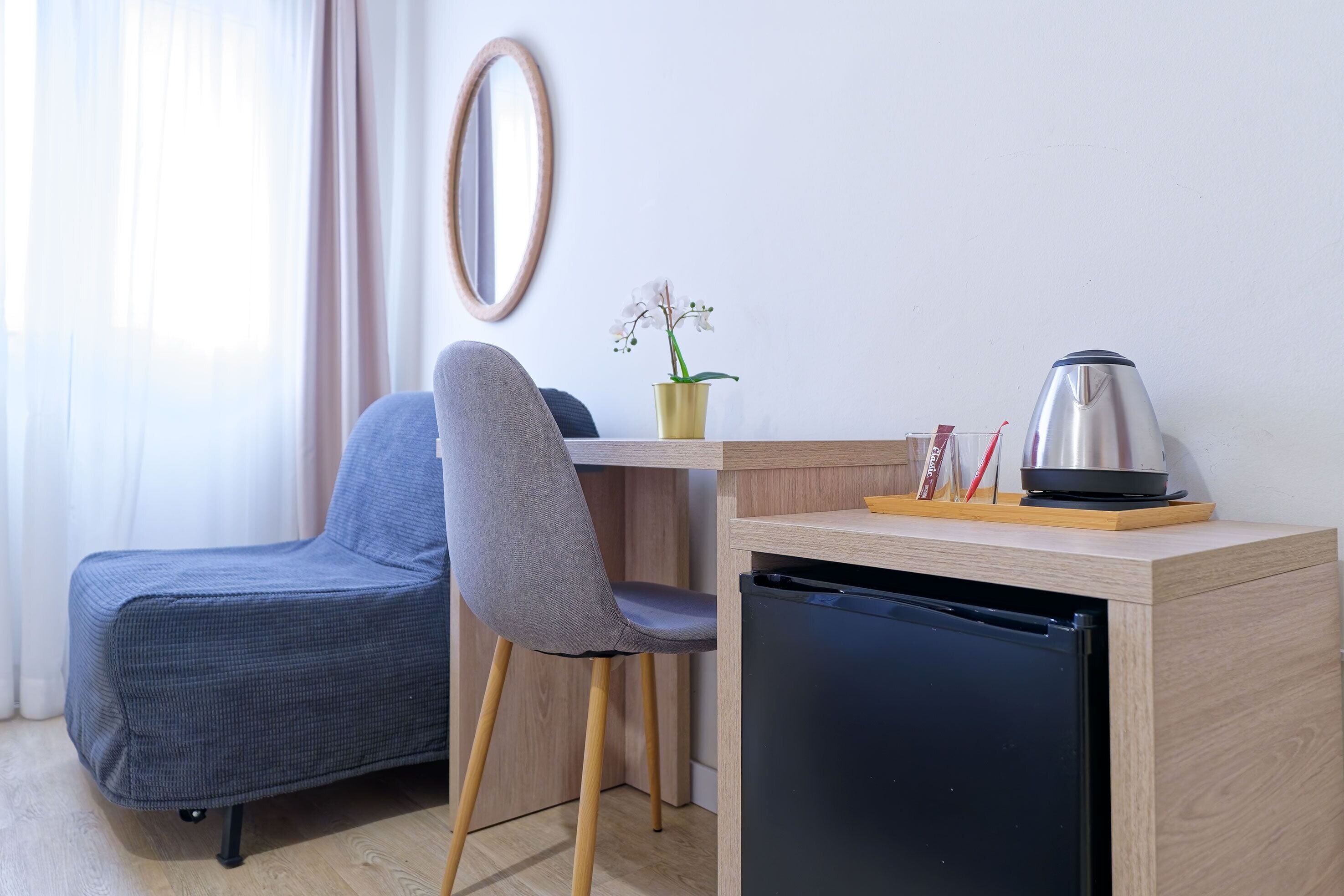 A compact room with a grey chair, a small wooden table, a black refrigerator, and a potted orchid.