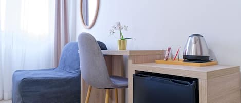 A compact room with a grey chair, a small wooden table, a black refrigerator, and a potted orchid.