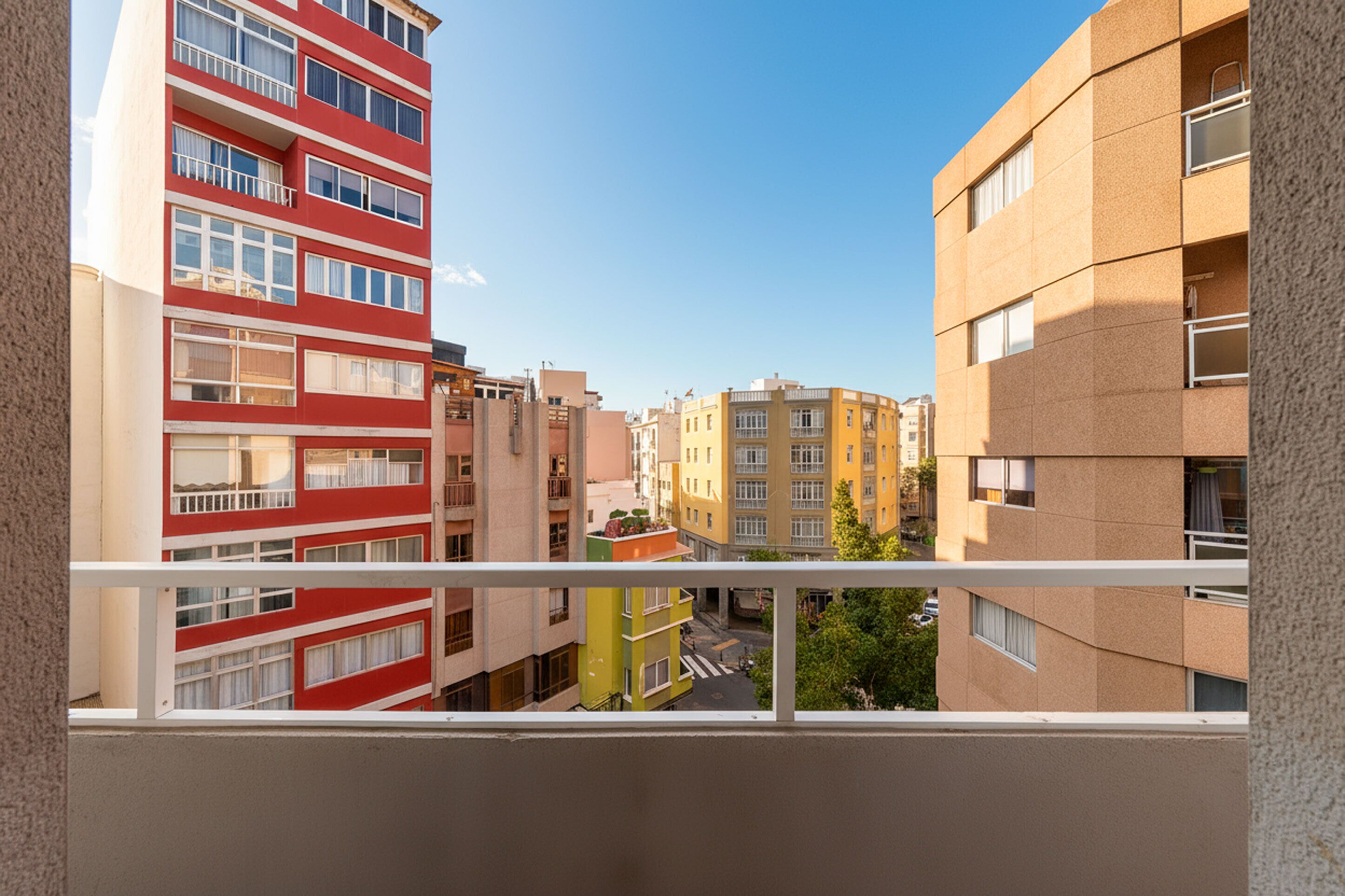 Une vue depuis un balcon donnant sur une rangée d’immeubles à plusieurs étages, chacun doté de balcons, une rue en contrebas et un ciel dégagé.