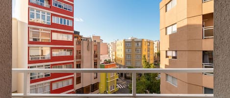 Vista desde un balcón sobre una hilera de edificios de varios pisos con balcones, una calle abajo y un cielo despejado.