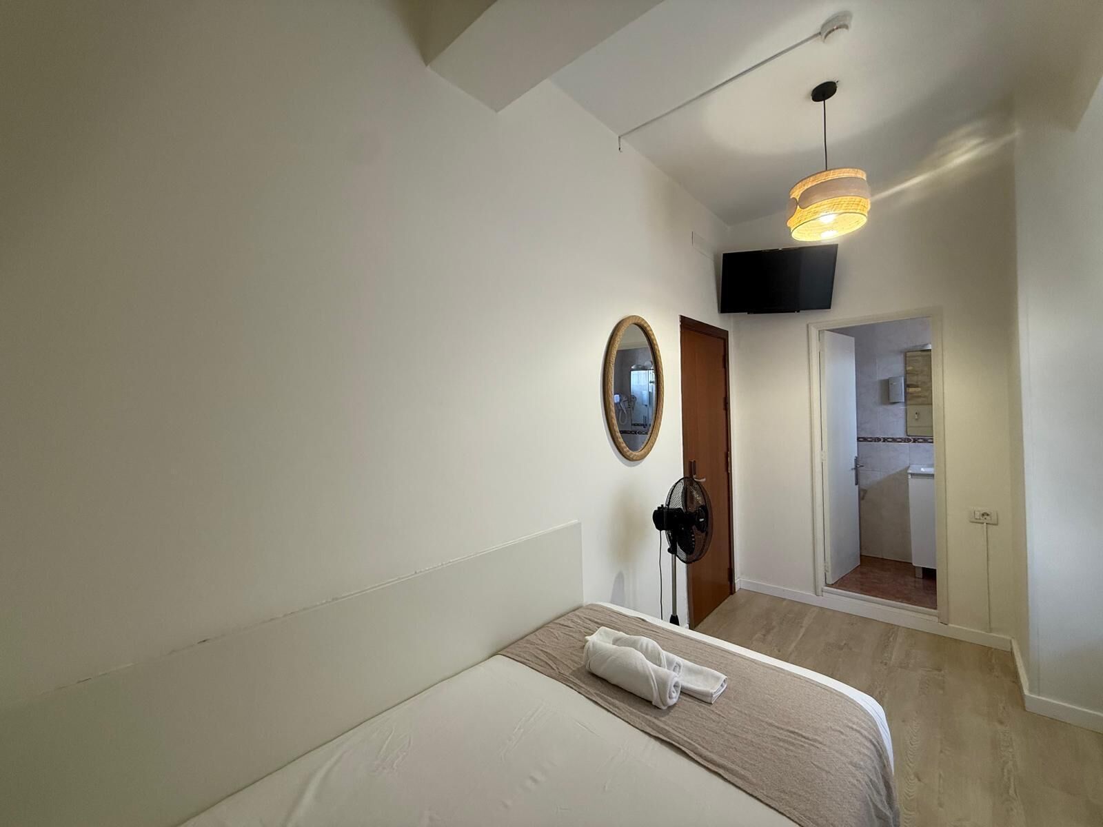 Un dormitorio con cama, espejo, ventilador de techo y televisor instalado en la pared.