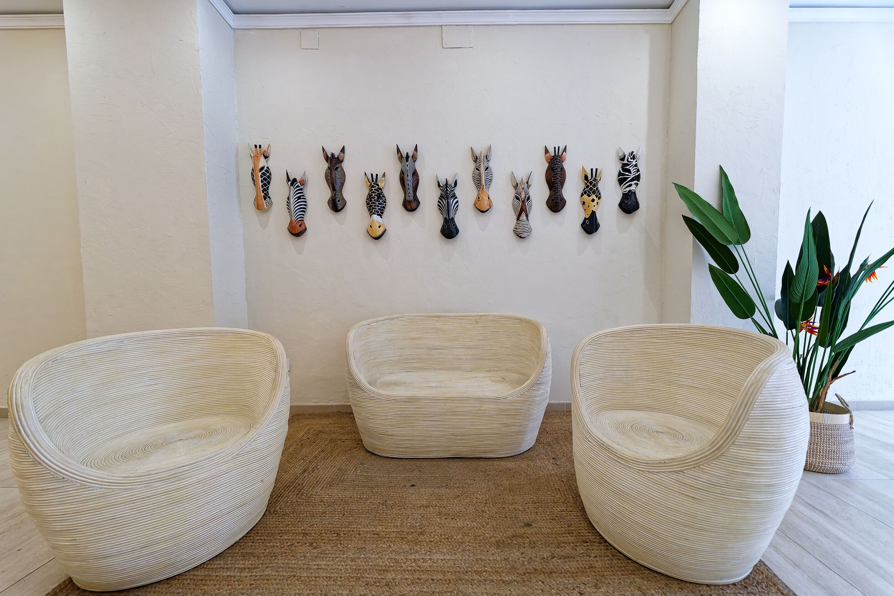 Une pièce comprenant trois chaises en osier, une décoration murale représentant une tête de zèbre et une plante en pot.