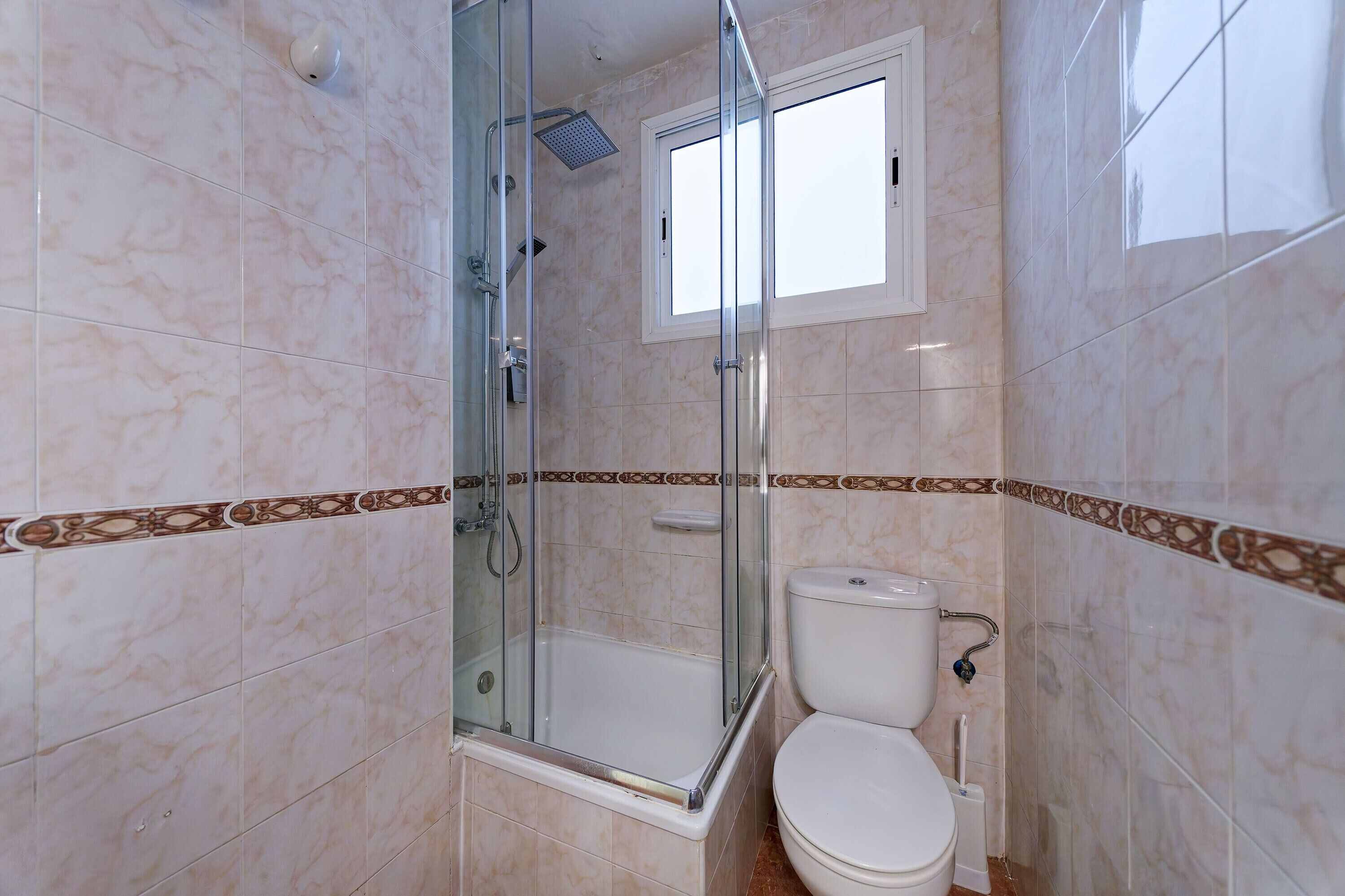 Un baño con ducha de vidrio, inodoro y ventana.