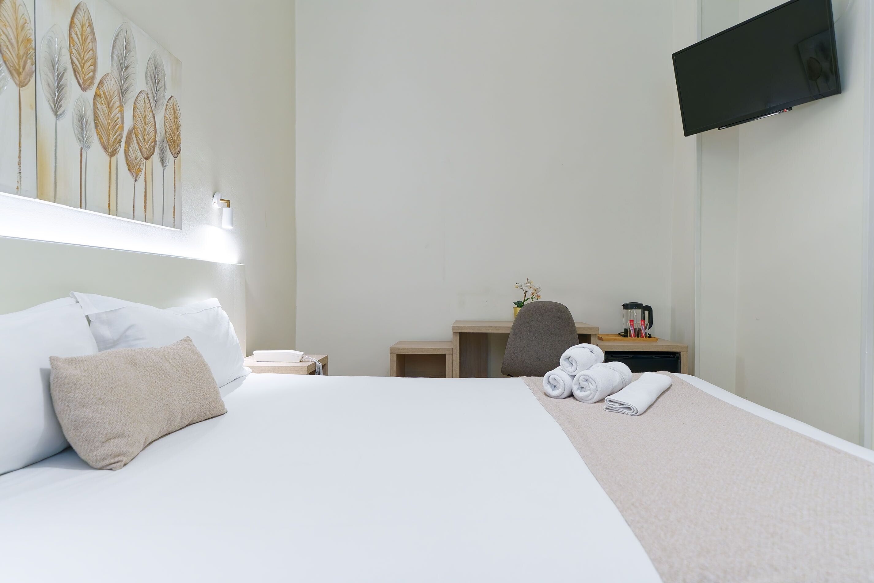 Habitación de hotel con cama, escritorio, silla, televisión y un cuadro en la pared.